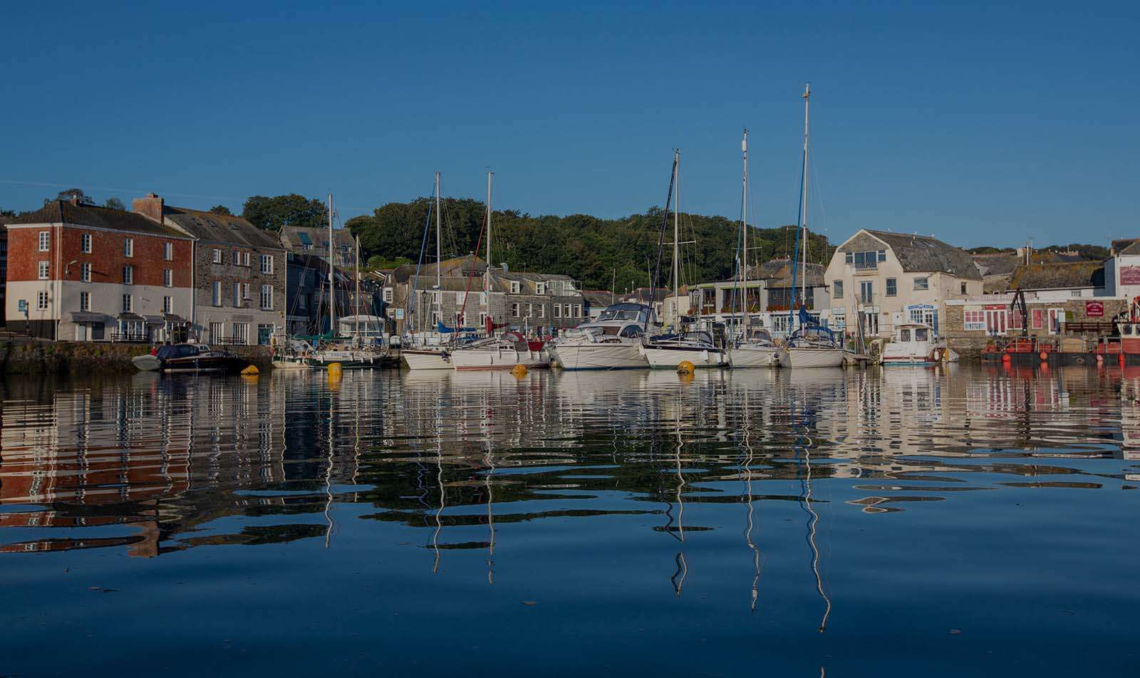 Padstow harbourfront and moored boats reflected in still water, North Cornwall