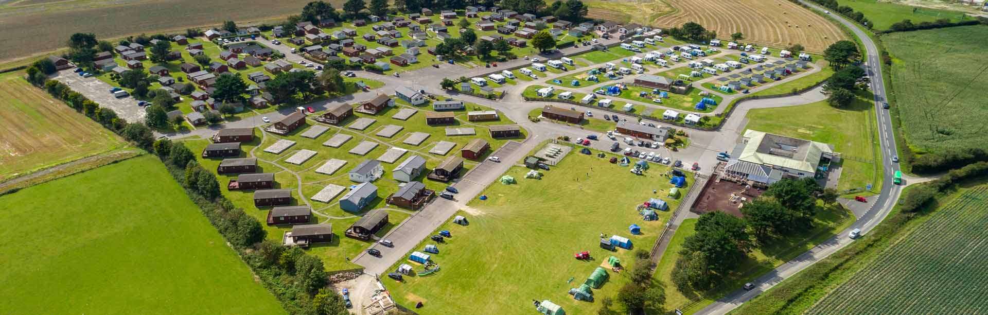 Aerial view of Atlantic Bays Holiday Park — lodge rows, the touring and tent field and facilities building set among St Merryn farmland