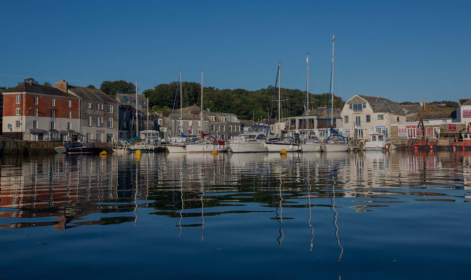 Padstow harbourfront houses and moored yachts reflected in the calm harbour water, Cornwall