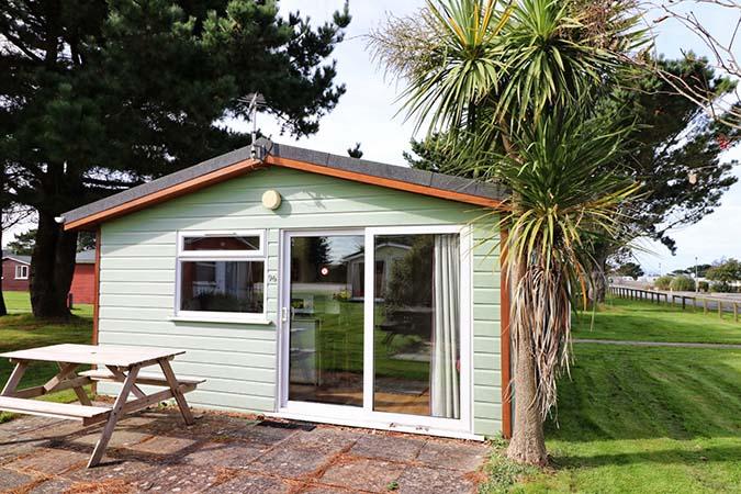 Green-painted Sun Cabin exterior with picnic bench at Atlantic Bays Holiday Park